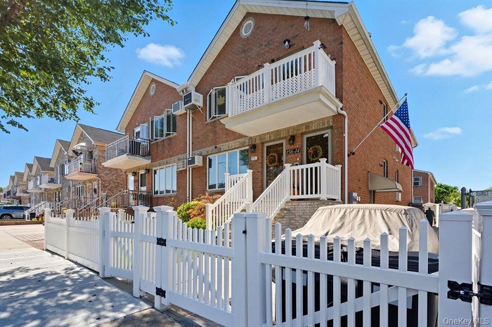 Traditional-style home featuring brick siding, a balcony, a fenced front yard, a gate, and a residential view