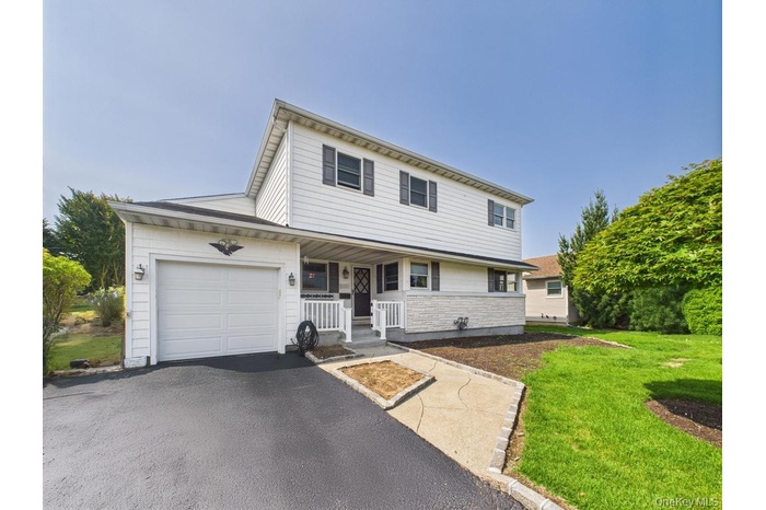 Traditional home with asphalt driveway, a front yard, a garage, a porch, and stone siding