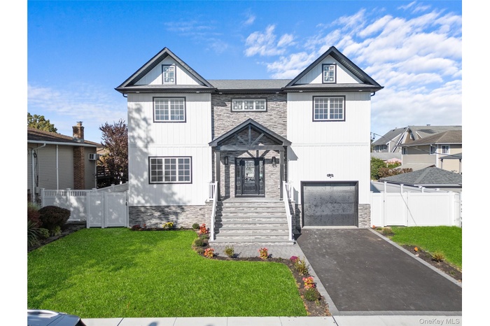 View of front facade with an attached garage, driveway, and stone siding