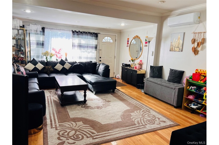 Living room with light wood-style floors, ornamental molding, and an AC wall unit