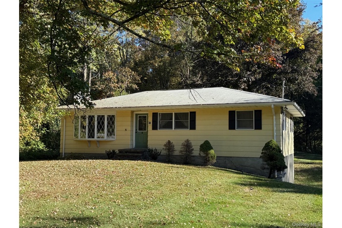 Ranch-style house with a front yard, entry steps, and view of wooded area