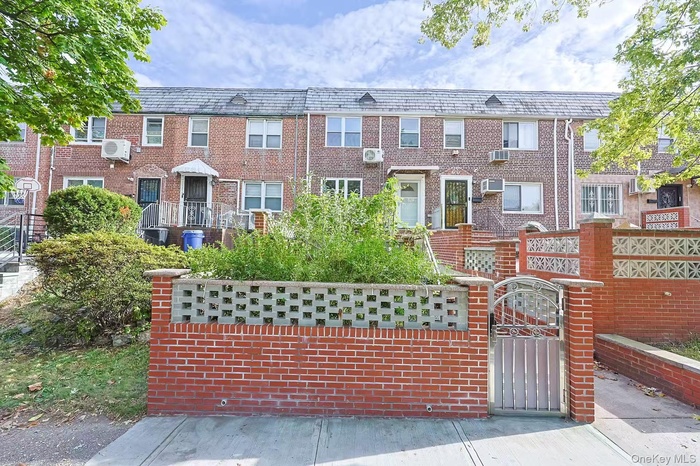 Colonial-style house with a gate, brick siding, and a wall mounted AC