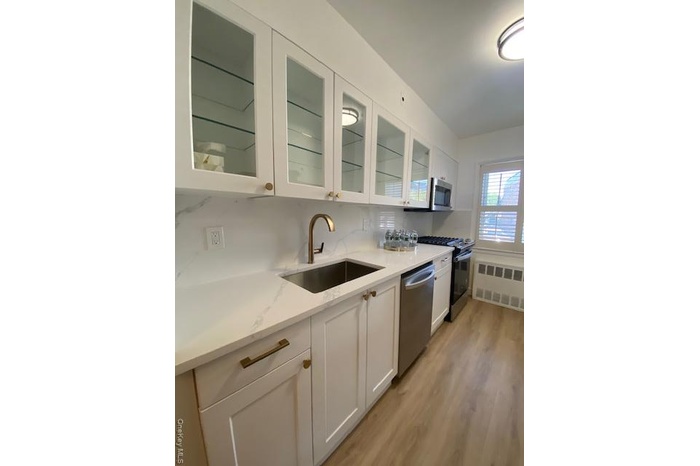 Kitchen featuring white cabinets, stove, radiator heating unit, light wood-style floors, and tasteful backsplash