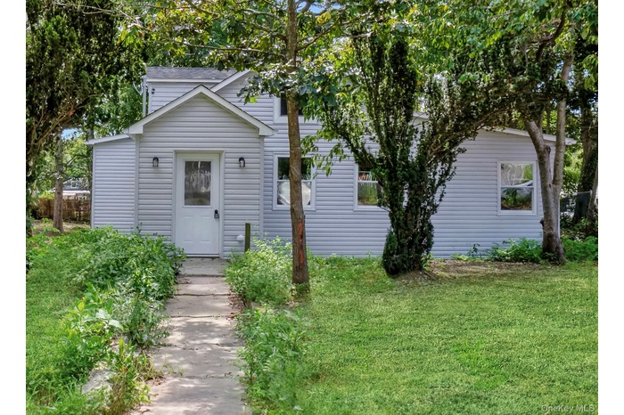 View of property hidden behind natural elements with a front lawn