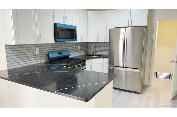 Kitchen with stainless steel appliances, backsplash, white cabinetry, light wood finished floors, and a peninsula
