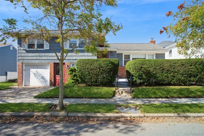 Split Level house featuring wood shingles and brick siding, Vinyl Siding, driveway, an attached garage, and a front lawn