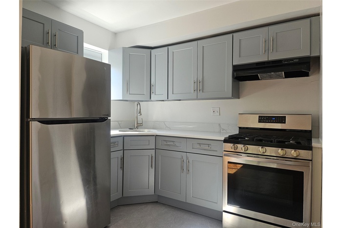 Kitchen featuring gray cabinets, appliances with stainless steel finishes, under cabinet range hood, and light stone countertops
