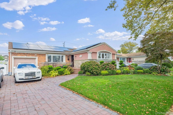 View of front of property featuring a front lawn, an attached garage, decorative driveway, roof mounted solar panels, and stone siding
