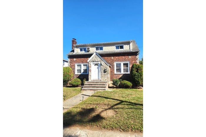 View of front of house featuring a chimney, a front lawn, and brick siding