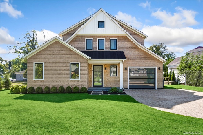 View of front of house with a front lawn, driveway, a garage, a metal roof, and board and batten siding