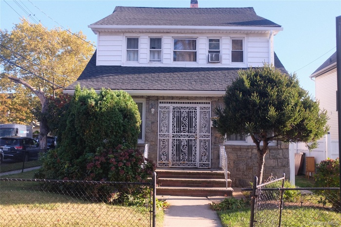 View of front facade featuring a fenced front yard, roof with shingles, a chimney, and stone siding
