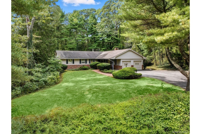 Ranch-style house featuring a chimney, a front yard, brick siding, asphalt driveway, and an attached garage