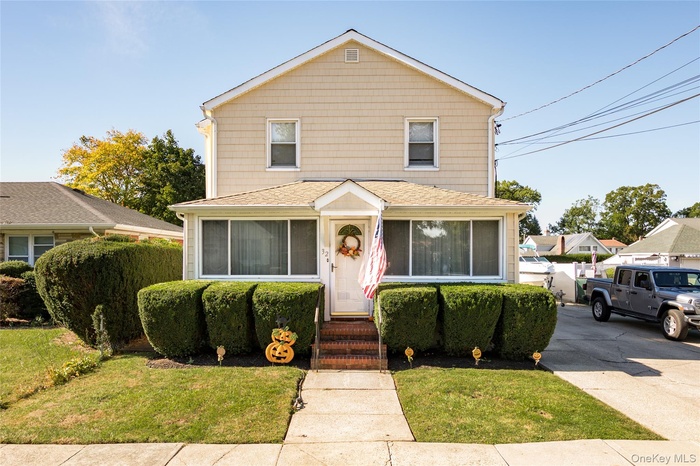 Traditional-style house with a front yard, roof with shingles, and a sunroom