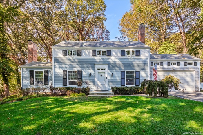 Colonial house with a chimney, a front lawn, a garage, and concrete driveway