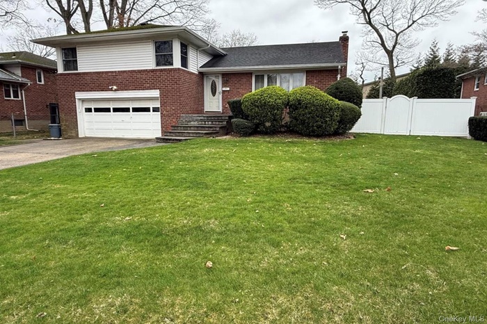 Tri-level home with concrete driveway, a chimney, brick siding, and a garage