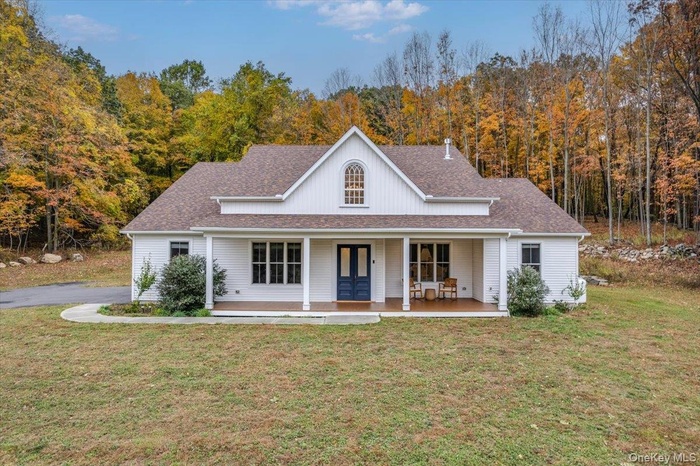 View of front of house featuring covered porch, a shingled roof, a front lawn, and a view of trees