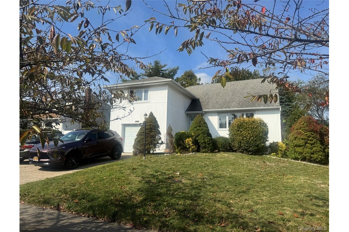 View of front of property featuring a front lawn, a shingled roof, and driveway