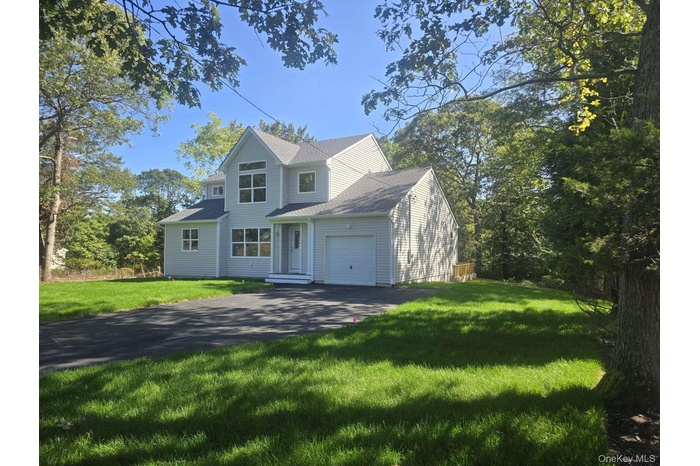 Traditional-style house featuring a front lawn, asphalt driveway, an attached garage, and a shingled roof