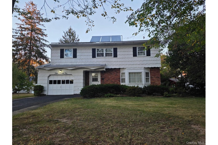 View of front facade with brick siding, a front yard, asphalt driveway, and an attached garage