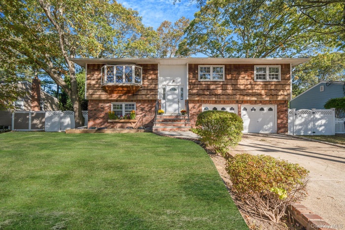 Raised ranch featuring brick siding, driveway, a garage, and a gate