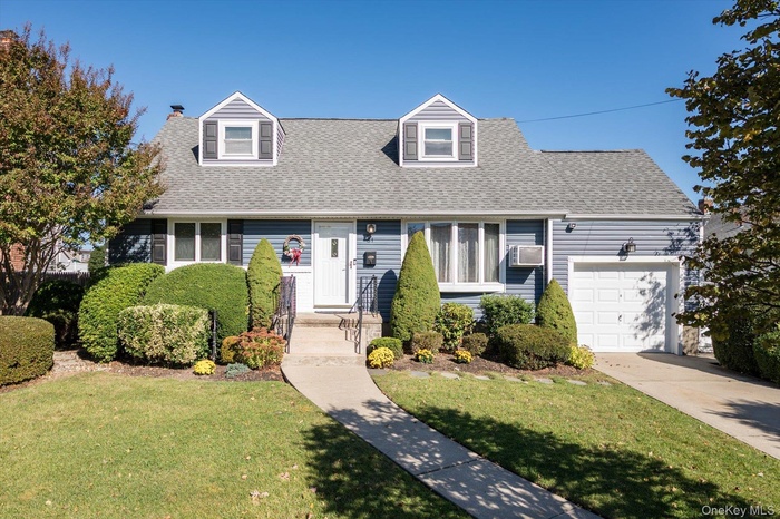 Cape cod house with roof with shingles, an attached garage, and a front yard