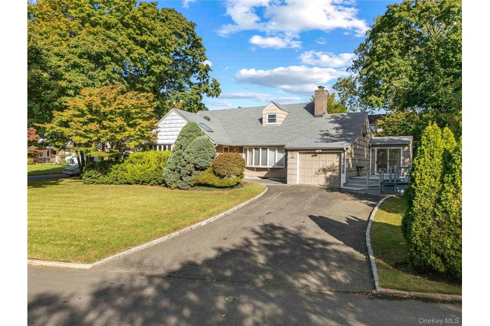 New england style home with a chimney, a front lawn, asphalt driveway, a shingled roof, and a garage