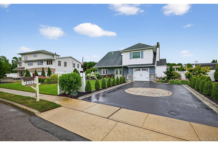View of front of property with a chimney, asphalt driveway, stone siding, a garage, and a front yard