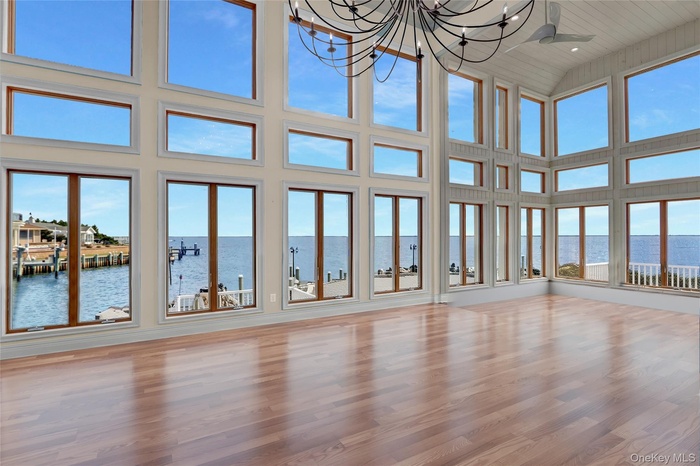 Virtually Staged Unfurnished living room featuring a water view, a towering ceiling, wood floors, a chandelier, and plenty of natural light