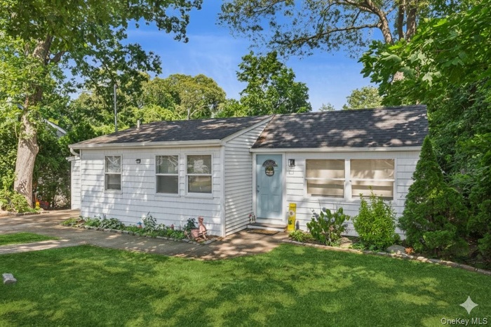 View of front facade featuring a front lawn, a shingled roof, and view of wooded area