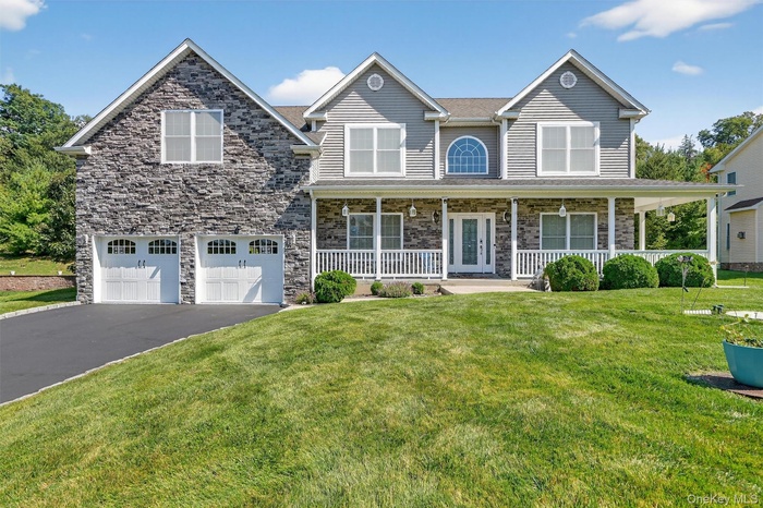 Traditional-style house featuring a porch, a front lawn, driveway, an attached garage, and stone siding