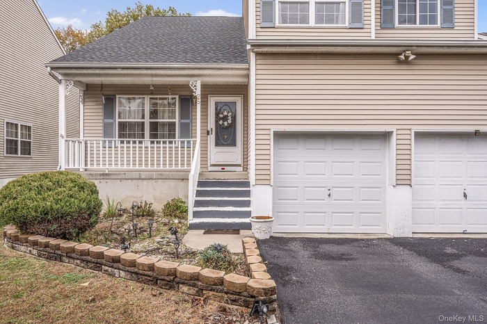 Property entrance featuring covered porch, roof with shingles, a garage, and driveway