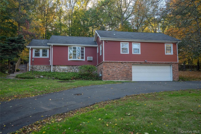 View of front facade with driveway, an attached garage, a front yard, and view of scattered trees