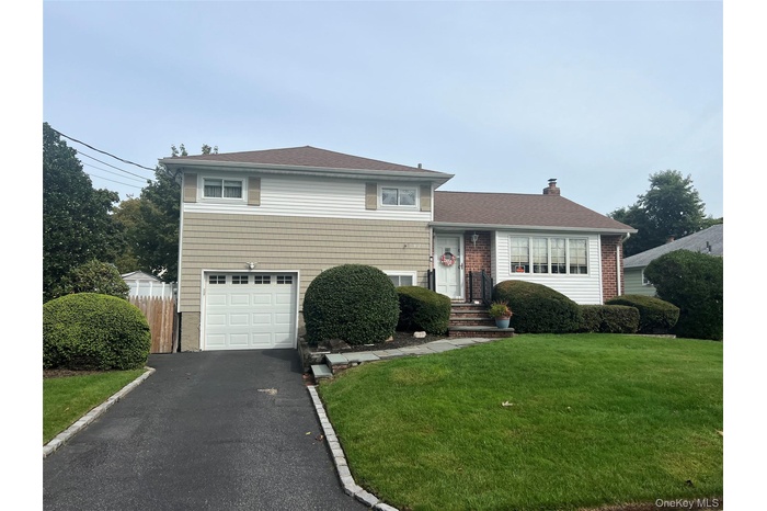Tri-level home featuring a garage, driveway, a chimney, brick siding, and roof with shingles