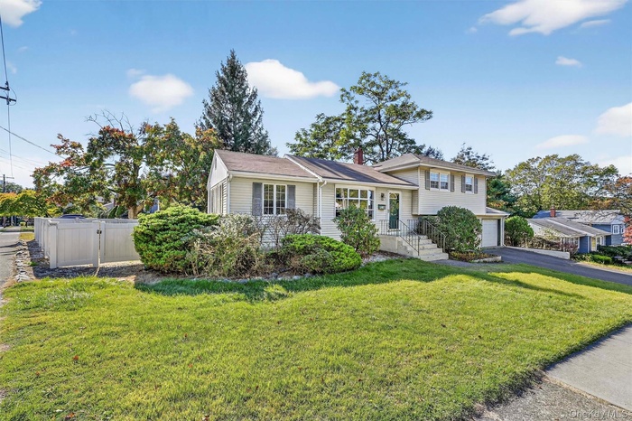 Split level home featuring a front lawn, asphalt driveway, a garage, and a chimney