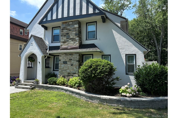 English style home featuring stone siding, stucco siding, a front lawn, and a shingled roof