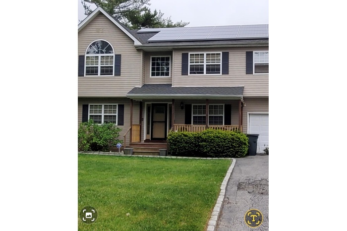 View of front of property with a porch, a front lawn, roof mounted solar panels, and driveway