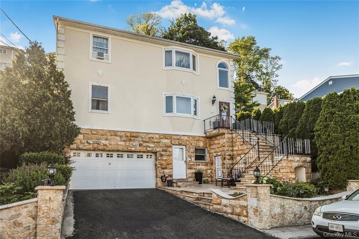 View of front of house featuring stucco siding, asphalt driveway, stairs, stone siding, and a garage