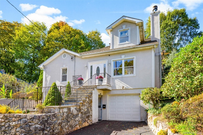View of front facade with stucco siding, a chimney, attached garage, and driveway