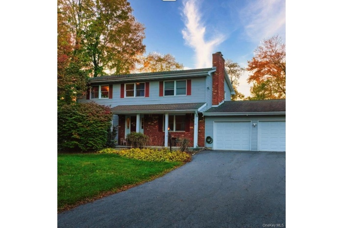 View of front of property featuring a porch, an attached garage, driveway, a chimney, and a front lawn