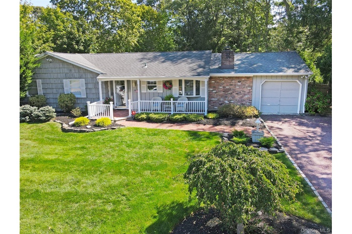 Ranch-style home with a chimney, covered porch, a shingled roof, and a front lawn