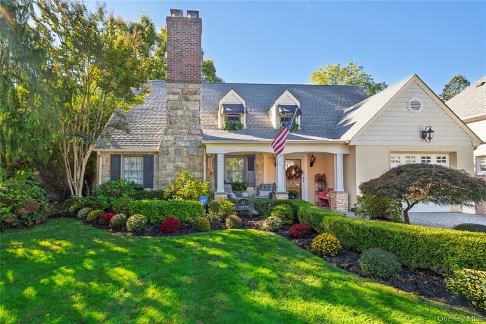 View of front of home featuring a porch, a chimney, a front lawn, stone siding, and stucco siding