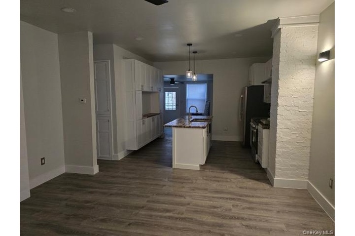 Kitchen with white cabinetry, dark wood finished floors, pendant lighting, stainless steel gas range, and an island with sink