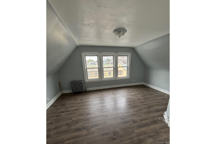 Additional living space featuring vaulted ceiling, dark wood-style floors, radiator, and a textured ceiling