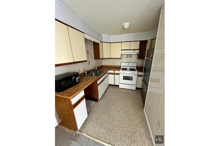 Kitchen with white range with gas stovetop, black microwave, freestanding refrigerator, brown cabinets, and under cabinet range hood