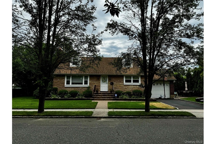Cape cod home featuring a front lawn, asphalt driveway, roof with shingles, and stone siding
