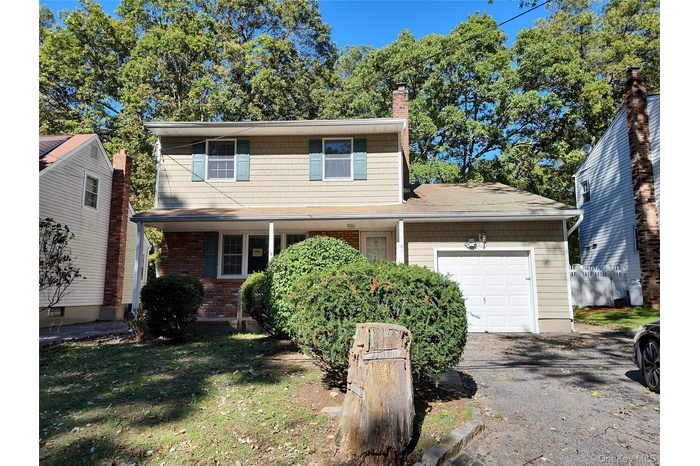 Traditional-style house featuring a garage, a chimney, a front lawn, driveway, and a porch