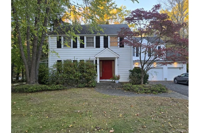 Colonial inspired home featuring a front yard, a garage, asphalt driveway, and a shingled roof