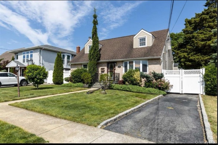 Cape cod home featuring a gate, brick siding, and a shingled roof