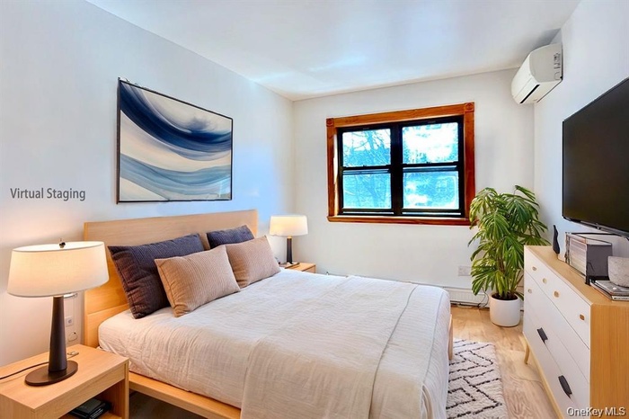Bedroom with light wood-type flooring and an AC wall unit