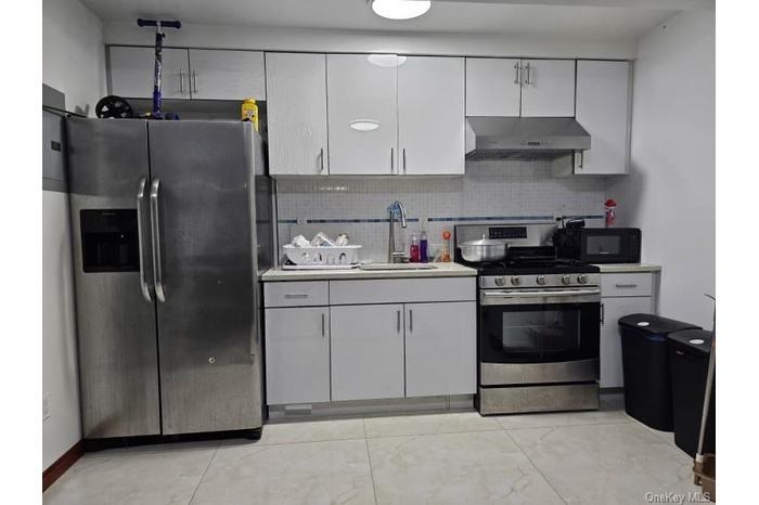 Kitchen featuring white cabinetry, stainless steel appliances, under cabinet range hood, light countertops, and tasteful backsplash